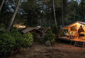 Beleuchtetes Safari-Bungalowzelt Classic am Abend im Wald bei Huttopia Landes Sud in Frankreich, Familie sitzt davor.