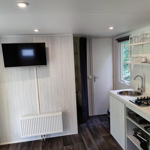 Intérieur douillet du Glamping Coco Sweet à Bospark De Brenkberg, Pays-Bas, avec cuisine et télévision.
