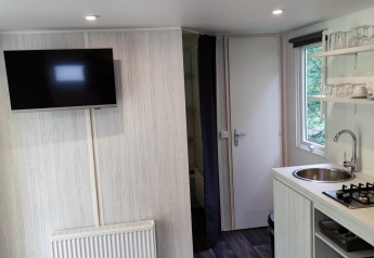 Intérieur douillet du Glamping Coco Sweet à Bospark De Brenkberg, Pays-Bas, avec cuisine et télévision.