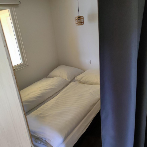 Petite chambre avec deux lits simples et draps blancs au Glamping Coco Sweet du Bospark De Brenkberg.