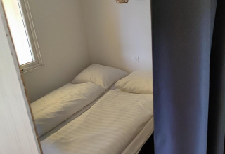 Pequeña área de dormitorio con dos camas individuales y sábanas blancas en Glamping Coco Sweet de Bospark De Brenkberg.