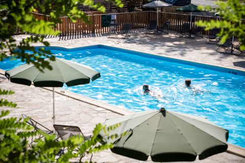 Piscina exterior con sombrillas verdes en Huttopia Gorges du Tarn, parque vacacional en Occitania, Francia.