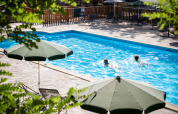 Outdoor swimming pool with green umbrellas at Huttopia Gorges du Tarn holiday park in Occitanie, France.