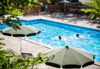Piscina exterior con sombrillas verdes en Huttopia Gorges du Tarn, parque vacacional en Occitania, Francia.