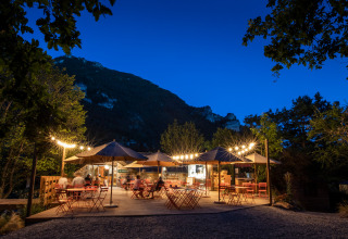 Outdoor café with string lights and mountain backdrop in the evening at Huttopia Gorges du Tarn, Occitanie, France.