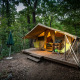 Safari telt Bungalow tent Classic på en træplatform i en skov, udstyret med stole, bord og paraply.