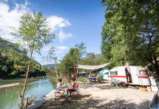 Campingplatz am Fluss in Huttopia Gorges du Tarn, Frankreich, mit Wohnwagen, Zelt und Urlaubsgästen.