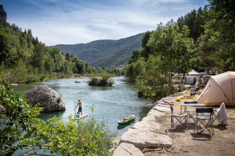 Campeggiatori godono di tende presso il fiume e attività acquatiche a Huttopia Gorges du Tarn, Occitania, Francia.