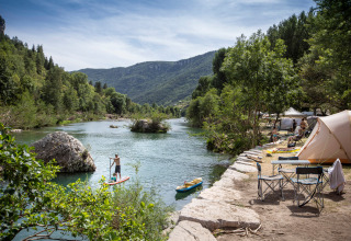Campeggiatori godono di tende presso il fiume e attività acquatiche a Huttopia Gorges du Tarn, Occitania, Francia.