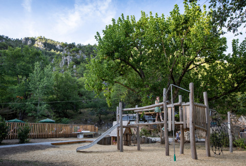 Parque infantil natural en Huttopia Gorges du Tarn, Occitanie, Francia, rodeado de montañas y árboles.