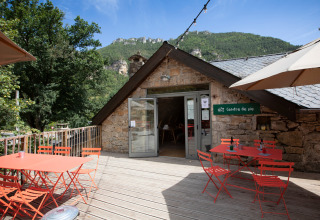 Buitenterras met rode tafels en stoelen aan Huttopia Gorges du Tarn vakantiepark in Occitanië, Frankrijk.