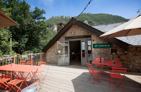 Terraza al aire libre con mesas y sillas rojas en Huttopia Gorges du Tarn, Occitanie, Francia.