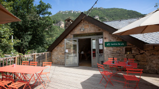 Terraza al aire libre con mesas y sillas rojas en Huttopia Gorges du Tarn, Occitanie, Francia.