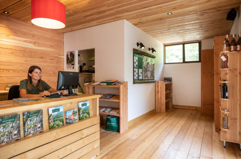 Rezeption mit Holzinterieur und freundlicher Mitarbeiterin am Computer im Huttopia Gorges du Tarn, Okzitanien, Frankreich.