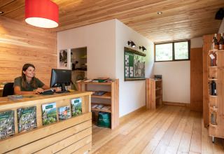 Recepción de madera con empleada sonriente en computadora en Huttopia Gorges du Tarn, Occitania, Francia.