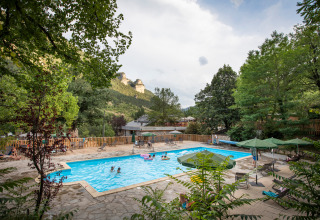 Swimmingpool på Huttopia Gorges du Tarn feriepark i Occitanie, Frankrig, omgivet af grønne bjerge og træer.