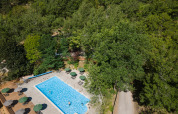 Luftfoto af en swimmingpool omgivet af grønne træer og parasoller på Huttopia Gorges du Tarn i Occitanie, Frankrig.