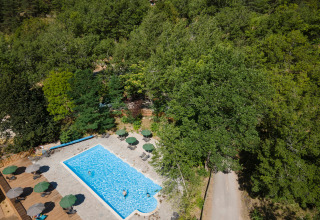 Luftaufnahme eines Pools mit Sonnenschirmen im Grünen im Huttopia Gorges du Tarn Ferienpark, Occitanie, Frankreich.