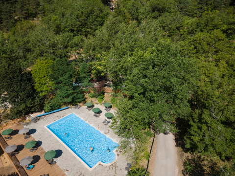 Vista aerea di una piscina con ombrelloni circondata da alberi a Huttopia Gorges du Tarn, Occitania, Francia.