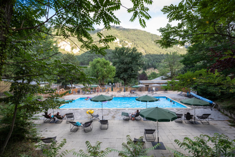 Piscina exterior con tumbonas y sombrillas en Huttopia Gorges du Tarn, parque de vacaciones en Occitania, Francia.