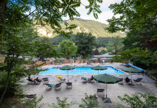 Swimmingpool med liggestole og parasoller i naturskønne omgivelser på Huttopia Gorges du Tarn, Occitanie, Frankrig.