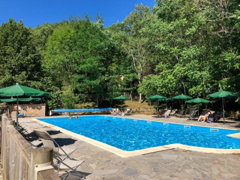 Outdoor swimming pool with lounge chairs and green umbrellas, surrounded by trees at Huttopia Gorges du Tarn, France.
