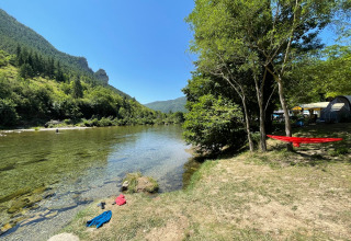 Campingplaats aan het water bij Huttopia Gorges du Tarn, Occitanië, Frankrijk, met bossen en bergen.