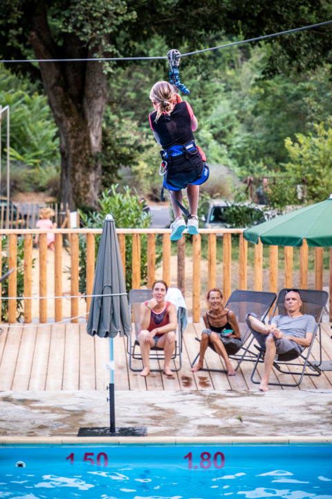 Un niño cruza en tirolesa sobre la piscina mientras la gente observa en Huttopia Gorges du Tarn, Occitanie, Francia.