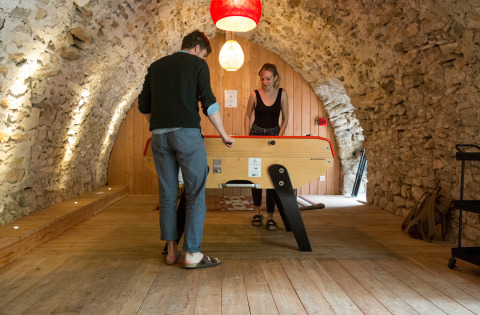 Two people play table football in a cozy stone-vaulted room at Huttopia Gorges du Tarn, Occitanie, France.