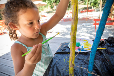 Een kind schildert buiten houten stokken in vakantiepark Huttopia Gorges du Tarn in Occitanië, Frankrijk.