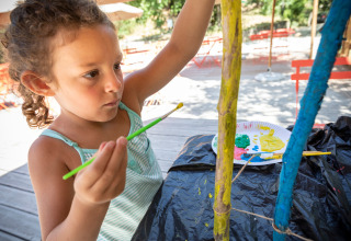 Een kind schildert buiten houten stokken in vakantiepark Huttopia Gorges du Tarn in Occitanië, Frankrijk.