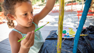 Una niña pinta palos de madera al aire libre en Huttopia Gorges du Tarn, un parque vacacional en Occitania, Francia.