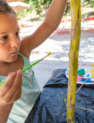 Una niña pinta palos de madera al aire libre en Huttopia Gorges du Tarn, un parque vacacional en Occitania, Francia.