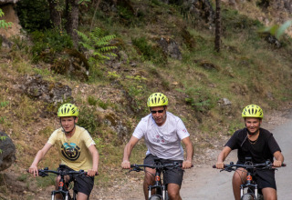 Drie personen fietsen in het groen bij Huttopia Gorges du Tarn vakantiepark in Occitanië, Frankrijk.