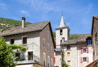 Sunny village square with shops and stone buildings near Huttopia Gorges du Tarn in Occitanie, France.