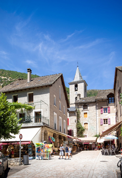 Plaza de pueblo soleada con comercios cerca de Huttopia Gorges du Tarn en Occitanie, Francia.