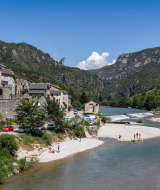 Río y playa concurrida junto a casas y montañas cerca de Massegros-Causses-Gorges, Occitania, Francia.