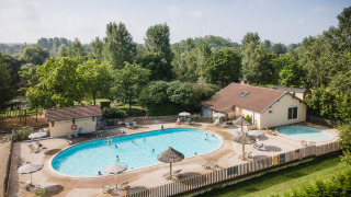 Piscina exterior con tumbonas y sombrillas en Huttopia La Plage Blanche en Bourgogne-Franche-Comté, Francia.