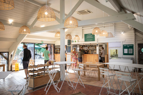 Personas esperan en una cafetería luminosa con muebles blancos en Huttopia La Plage Blanche, Francia.