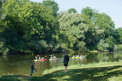 Niños observan a personas remando en kayak en un río rodeado de árboles verdes en Bourgogne-Franche-Comté.