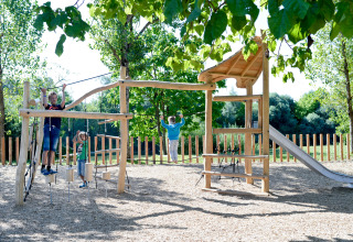 Children play on a wooden playground with climbing structures and a slide at Huttopia La Plage Blanche, France.