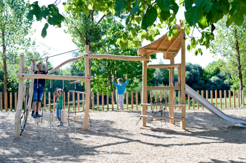 Children play on a wooden playground with climbing structures and a slide at Huttopia La Plage Blanche, France.
