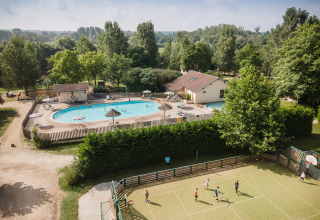 Aerial view of Huttopia La Plage Blanche holiday park in France featuring a pool, sports court, and greenery.