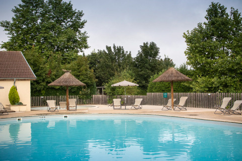 Piscina al aire libre con tumbonas y sombrillas en Huttopia La Plage Blanche, Bourgogne-Franche-Comté, Francia.