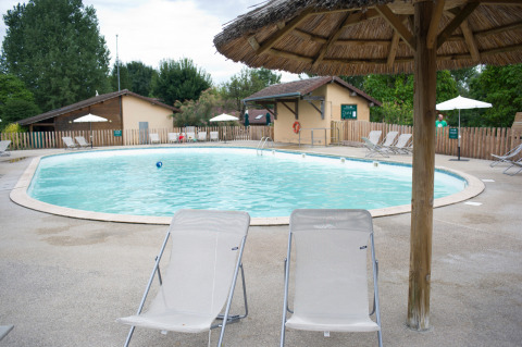 Piscina con tumbonas y sombrillas de paja en Huttopia La Plage Blanche, Bourgogne-Franche-Comté, Francia.