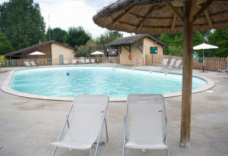 Piscina con tumbonas y sombrillas de paja en Huttopia La Plage Blanche, Bourgogne-Franche-Comté, Francia.