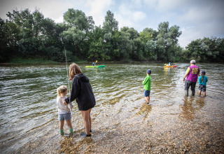 Gezinnen genieten van vissen en kajakken aan de rivier in vakantiepark Huttopia La Plage Blanche in Frankrijk.