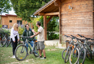Mensen staan met fietsen bij een houten hut in vakantiepark Huttopia La Plage Blanche in Frankrijk.