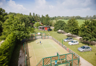 Children play on a sports court surrounded by green trees and parked cars at Huttopia La Plage Blanche, France.
