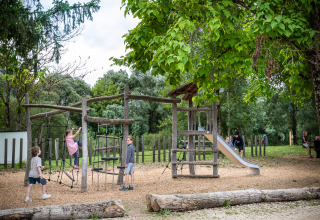 Kinderen spelen op een houten speelplein omgeven door bomen in Huttopia La Plage Blanche, Bourgogne-Franche-Comté.